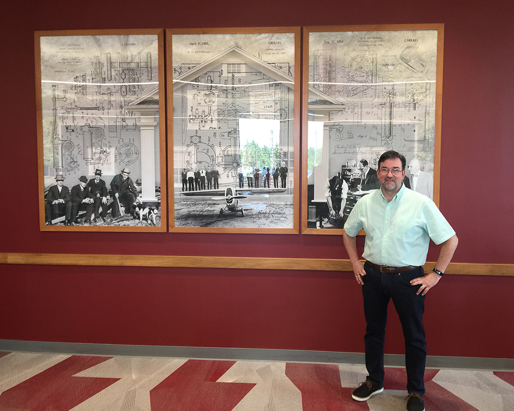 Dan Cleary of Cleary Creative Photography standing in front of at piece Kettering, Deeds and Delco at Dayton Metro Library Wilmington-Stroop branch