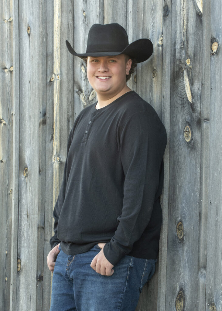 High School Senior portrait of boy leaning against old gray barn by Cleary Creative Photography
