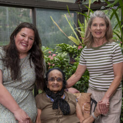 Three generations of women smiling in a greenhouse surrounded by tropical plants.