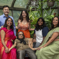 Multigenerational Indian family posing together in a greenhouse garden, smiling at the camera.