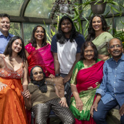 A large Indian family posing together in a greenhouse, smiling at the camera.